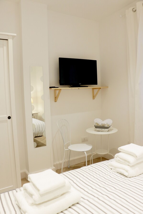 A hotel room with a bed, a television mounted on a wall, a small round table, a chair, and a mirror.