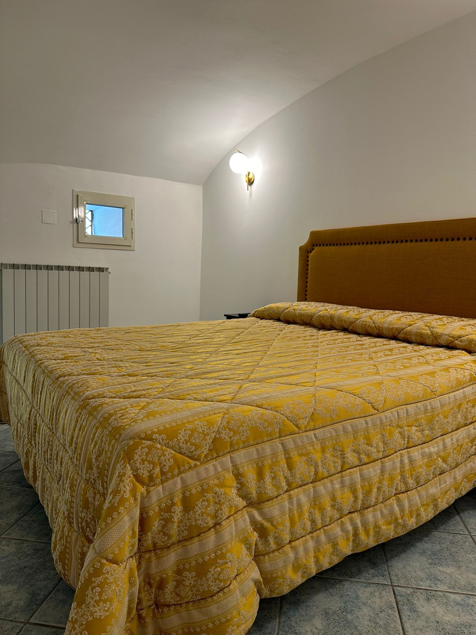 A bedroom with a bed, a window, a radiator, and a light fixture.