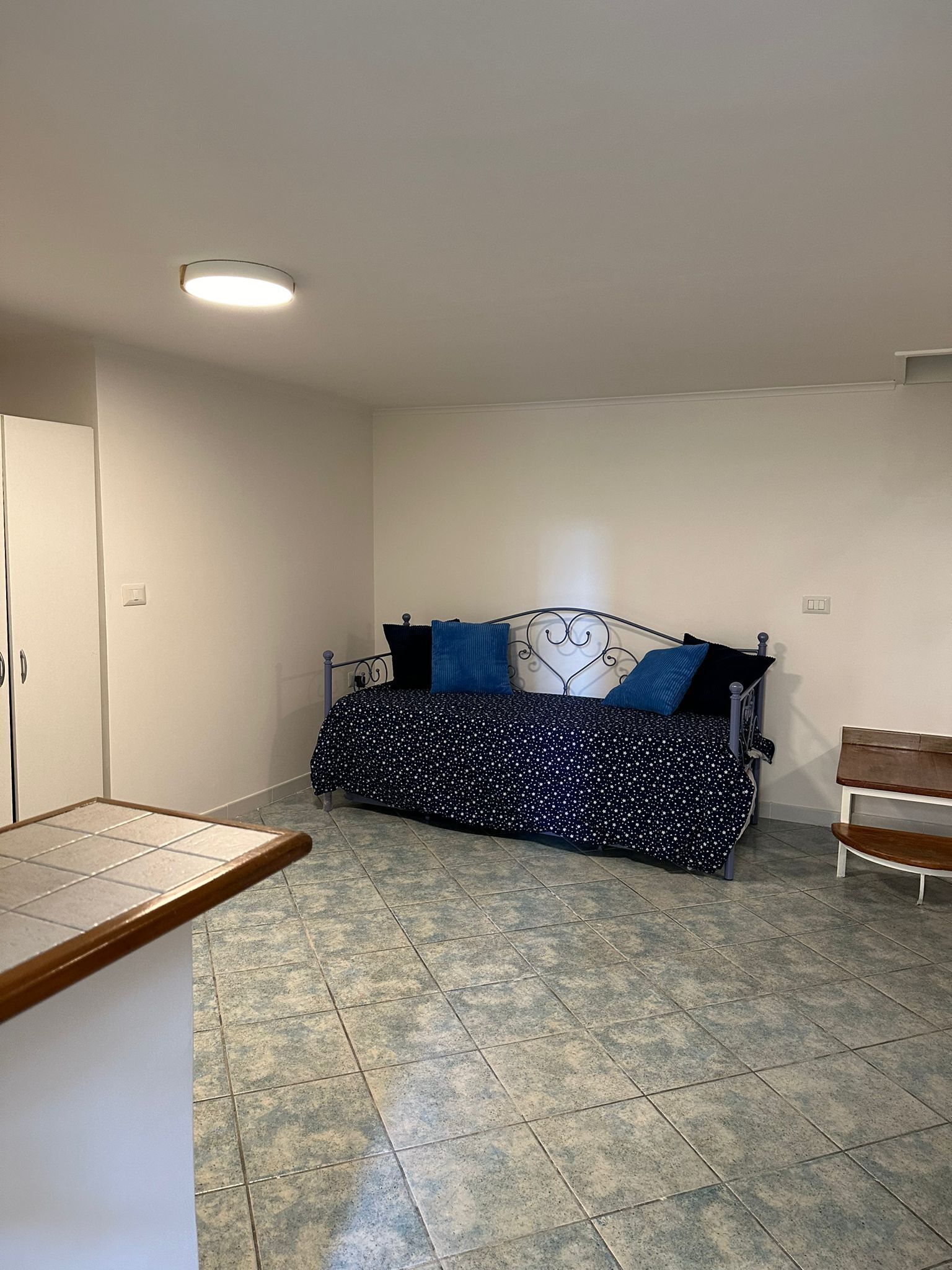 A room with a bed, a bench, a tiled floor, and a ceiling light.