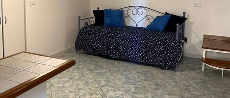 A room with a bed, a bench, a tiled floor, and a ceiling light.