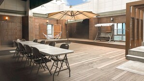 Un espace extérieur aménagé en terrasse, avec une longue table et des chaises, un hamac et un coin salon abrité.