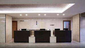 Un espace d’accueil moderne avec trois comptoirs d’accueil de couleur sombre, un plafond à lambris et un éclairage encastré.
