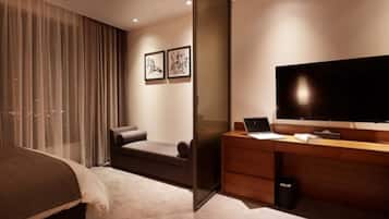 A modern hotel room with a bed, a desk with a laptop, a TV, and two framed pictures on the wall.