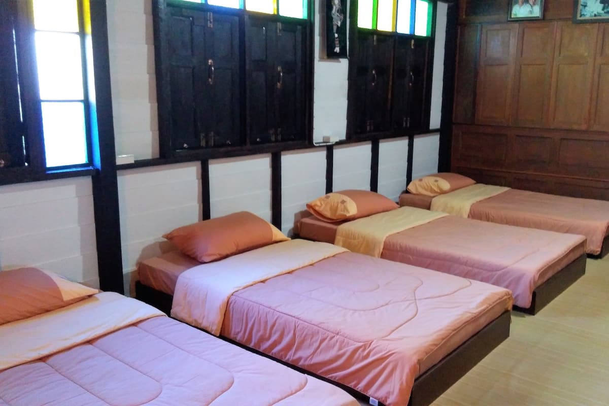 Ein Zimmer mit vier nebeneinanderstehenden Betten, Holzwänden und einem Fenster mit Jalousien.