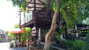 Un espace extérieur abrité, doté d’une terrasse en bois, de plantes en pot et d’un parasol rouge.