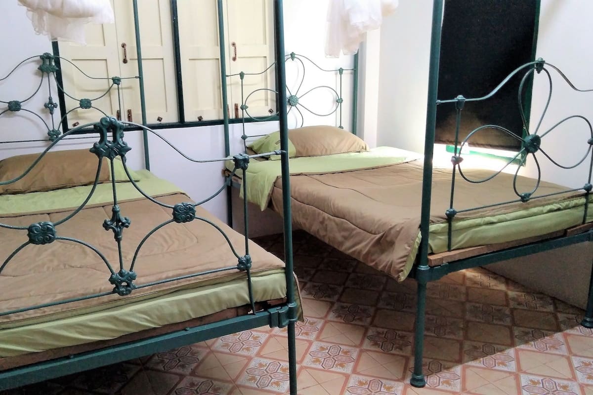 Zwei Etagenbetten aus Metall mit grünen Rahmen und beiger Bettwäsche in einem Zimmer mit gemusterten Bodenfliesen.