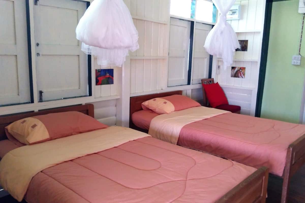 Ein Zimmer mit zwei Betten, beide mit hölzernen Kopfteilen, und einem roten Sessel.
