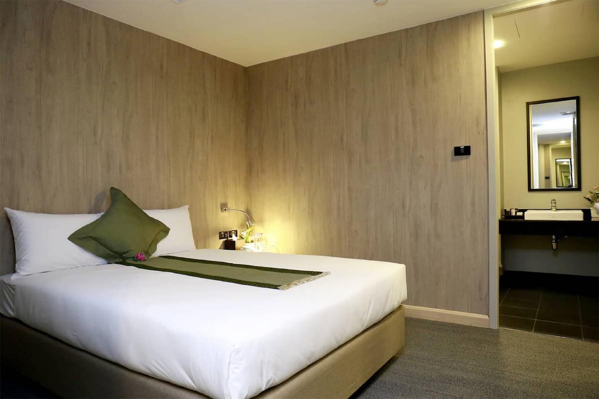 A hotel room with a large bed, a bedside table with a lamp, a mirror, and a bathroom with a sink and mirror.