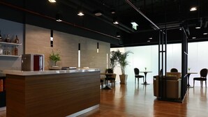 Un área de recepción moderna con un mostrador de madera, zonas de estar y vistas al exterior a través de amplios ventanales.