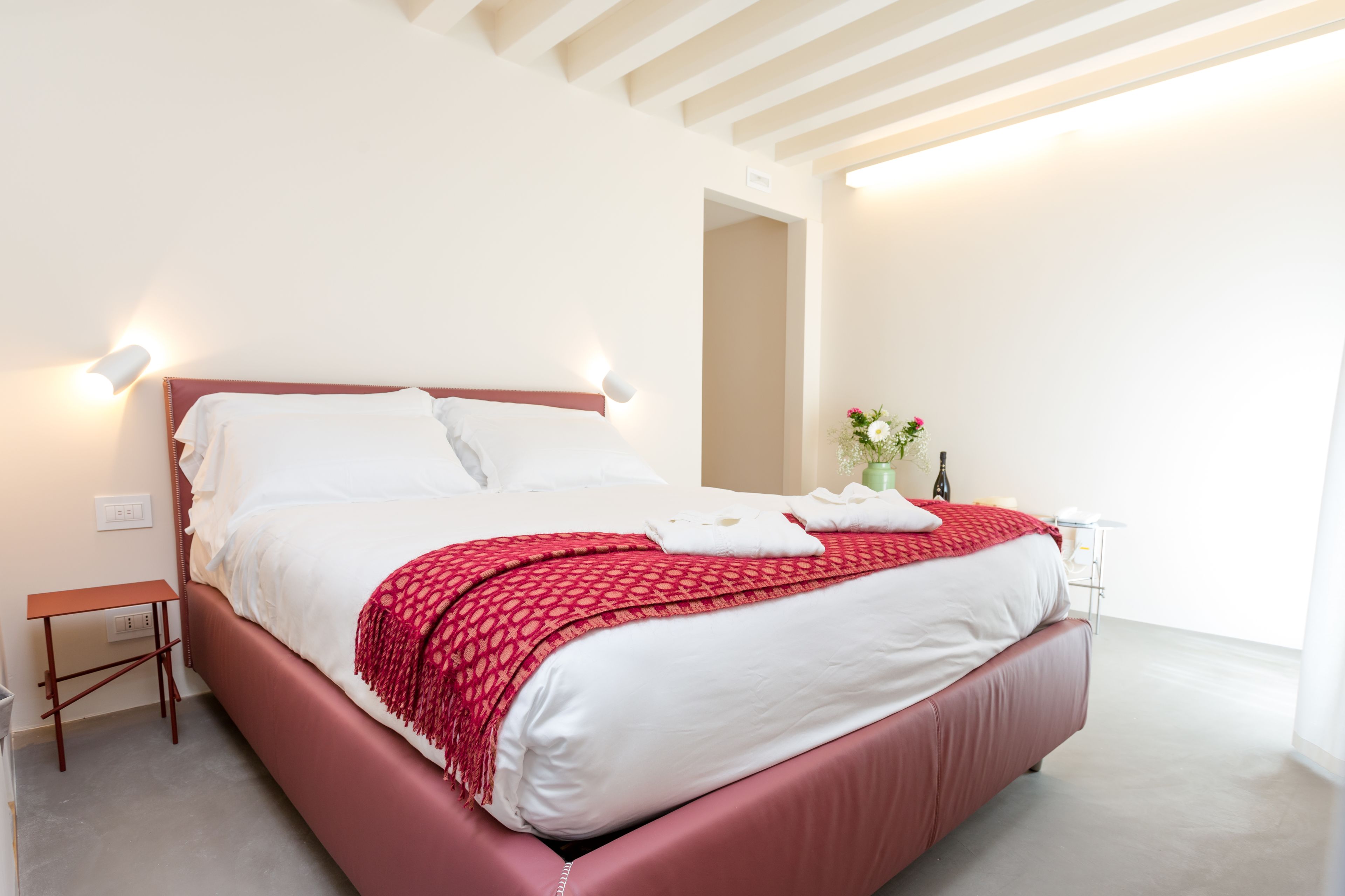 A modern bedroom with a large bed, a bedside table, a nightstand, and a vase with flowers.