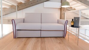 Una habitación moderna con un sofá de color claro, una mesita con una botella y un ventilador de techo.