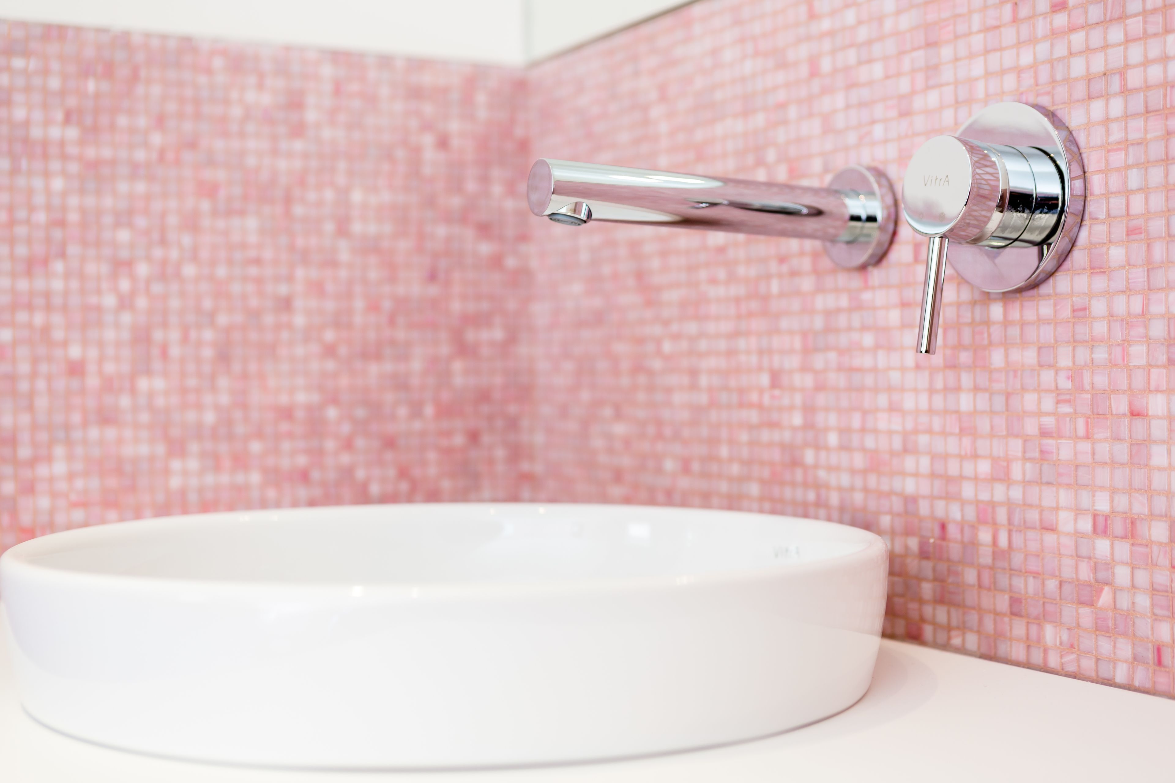 A bathroom with a white sink and a chrome faucet mounted on a pink mosaic tile wall.