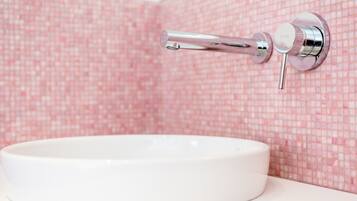 A bathroom with a white sink and a chrome faucet mounted on a pink mosaic tile wall.