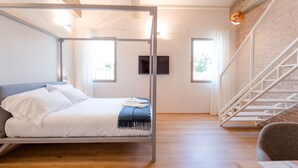 Un dormitorio moderno con estructura de cama metálica, piso de madera, una escalera y un televisor de pantalla plana en la pared.