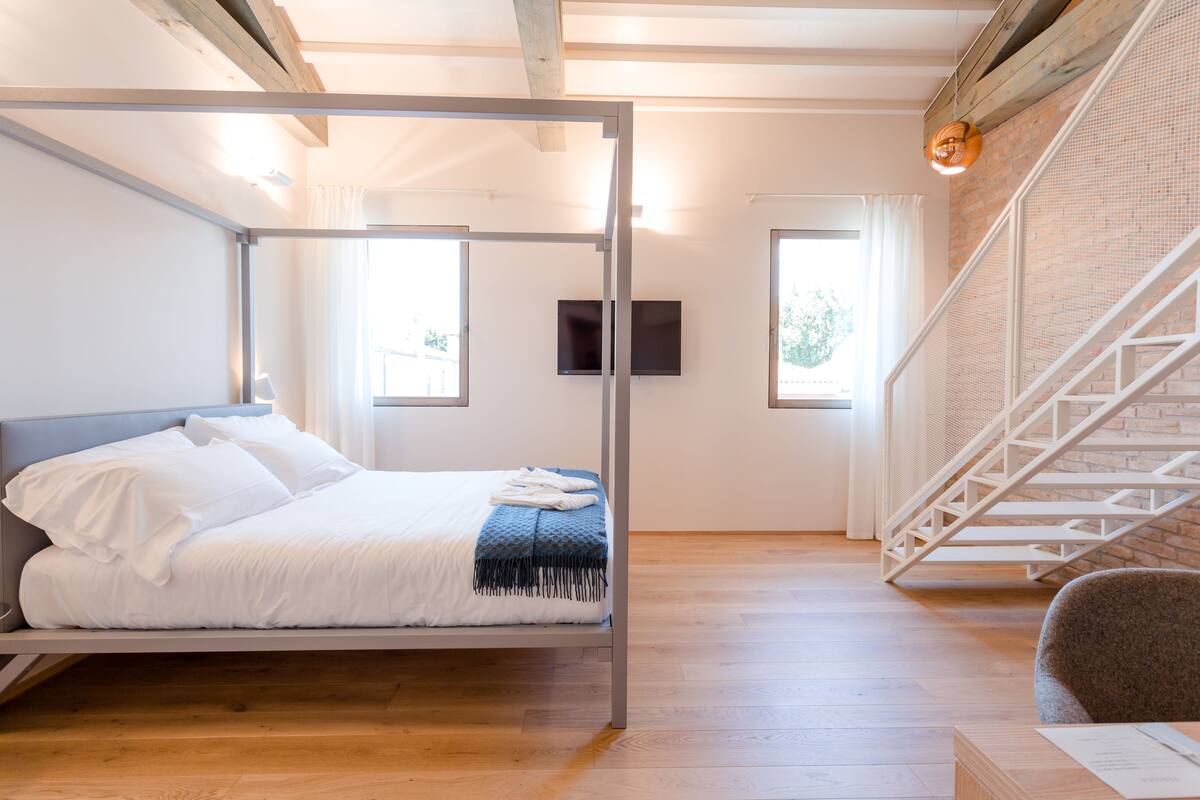 Un dormitorio moderno con estructura de cama metálica, piso de madera, una escalera y un televisor de pantalla plana en la pared.
