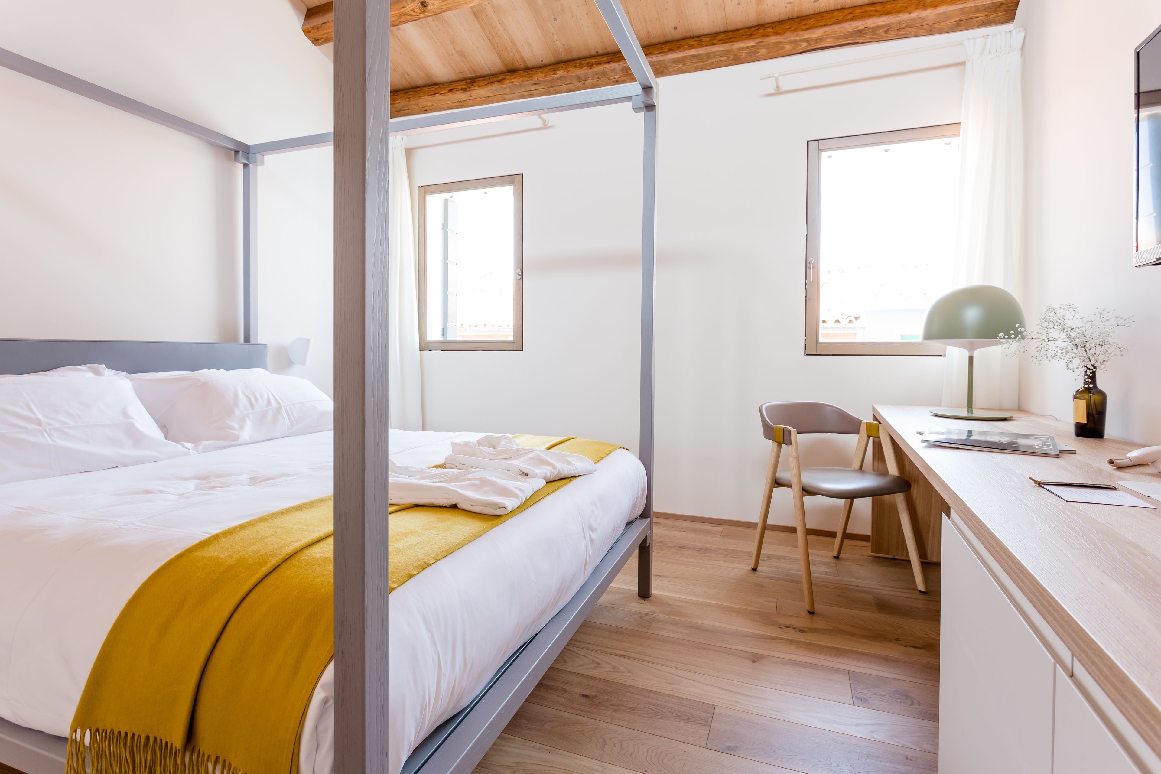 A bedroom with a bed, a desk, and two windows.
