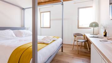 A bedroom with a bed, a desk, and two windows.