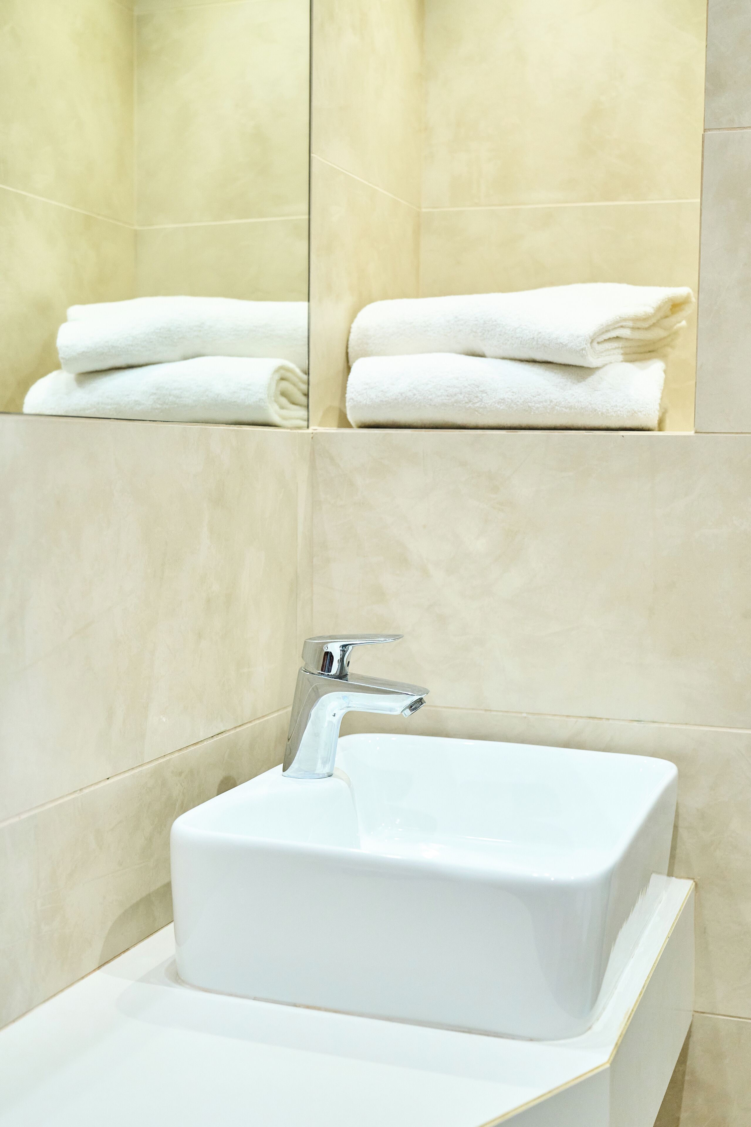 A bathroom with a white sink, a mirror, and a towel rack with folded towels.