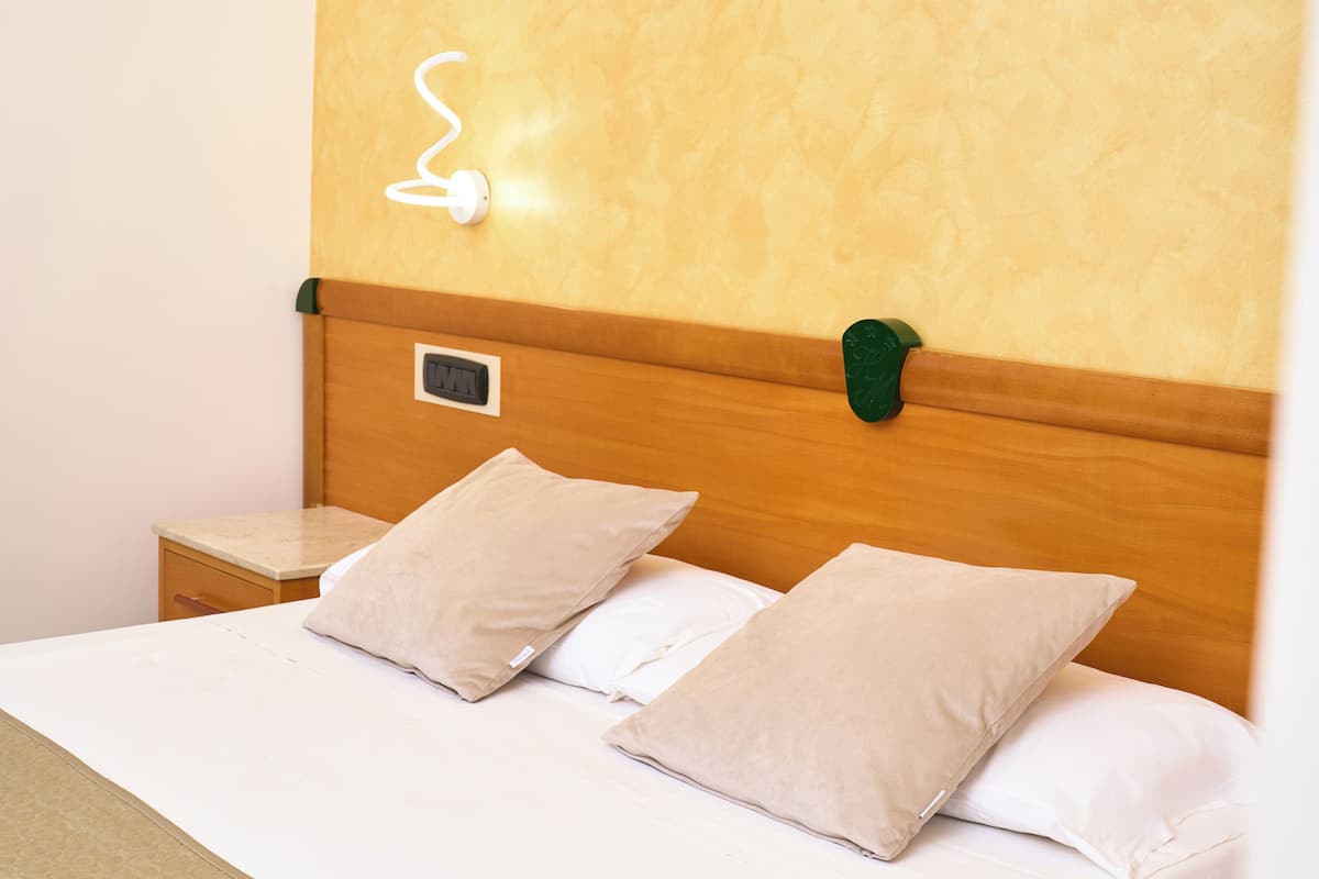 A neatly made bed with two beige pillows, a wooden headboard, a bedside table, and a wall socket.