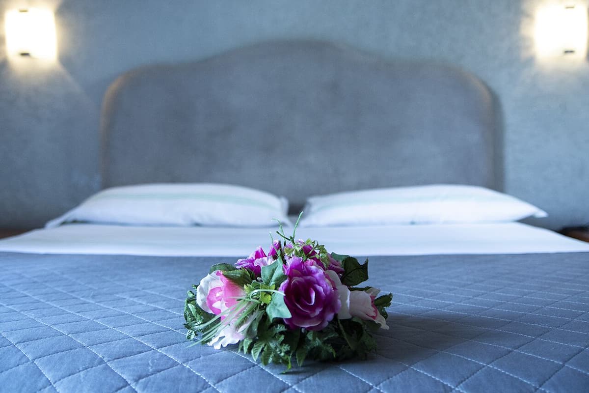A bed with a quilted blue bedspread and a floral arrangement on it.
