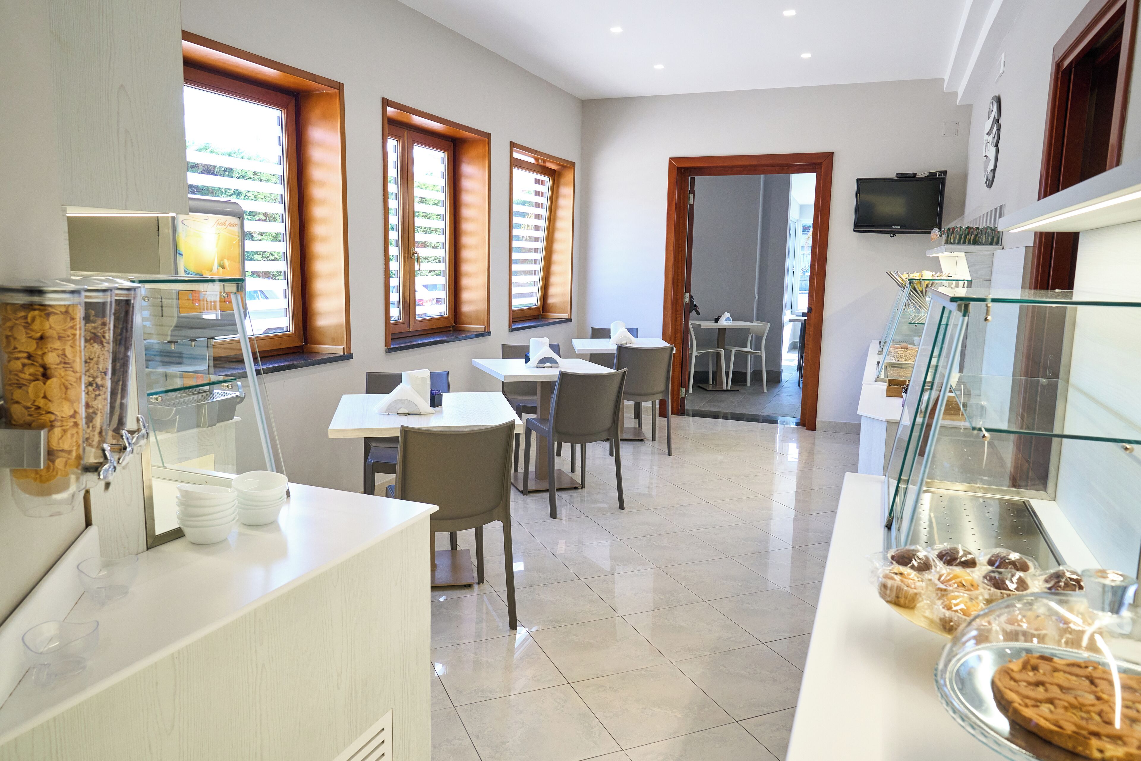 A modern dining area with a buffet setup, including a glass display case with pastries and a counter with a coffee machine.
