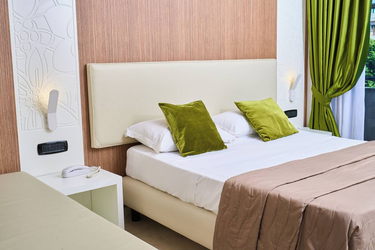 A neatly made bed with white and green pillows, a beige headboard, and a brown bedspread.