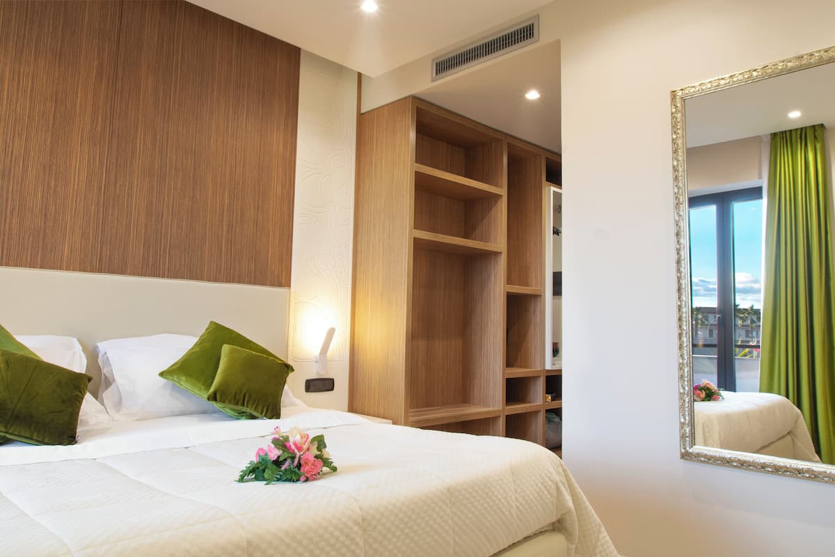 A hotel room with a bed, a large mirror, a wardrobe, and a view of the city through the window.