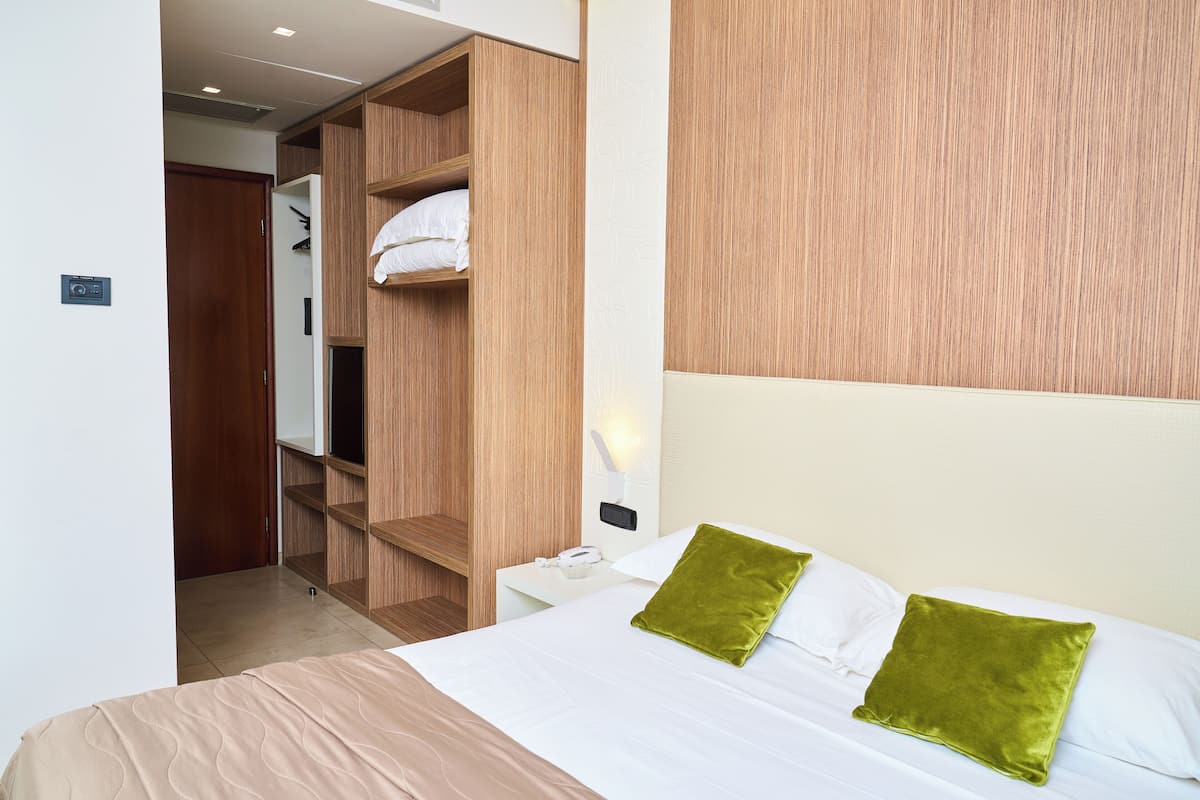 A hotel room with a bed, a wooden wardrobe, a nightstand, and a wall-mounted light.