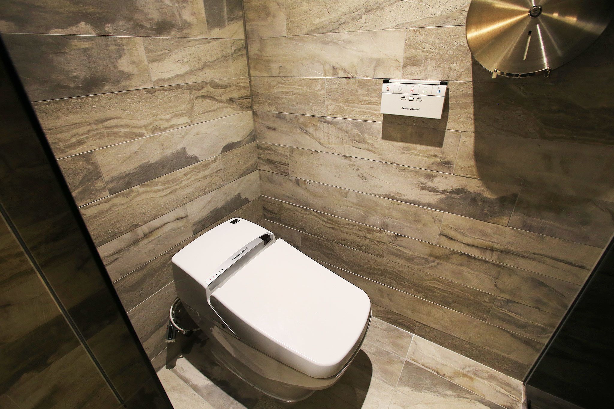 Un baño moderno con pared y suelo de mármol, un inodoro blanco y un panel de control instalado en la pared.