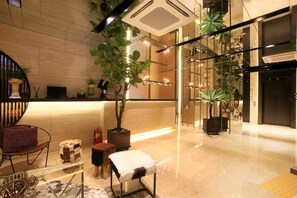 Een moderne lobby met een receptiebalie, zithoek en potplanten.