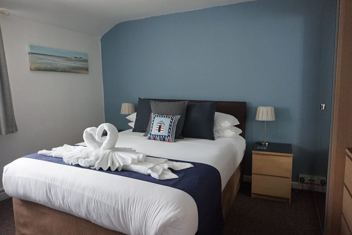Una habitación de hotel con una cama bien hecha, una mesita de noche con una lámpara y una pared azul.