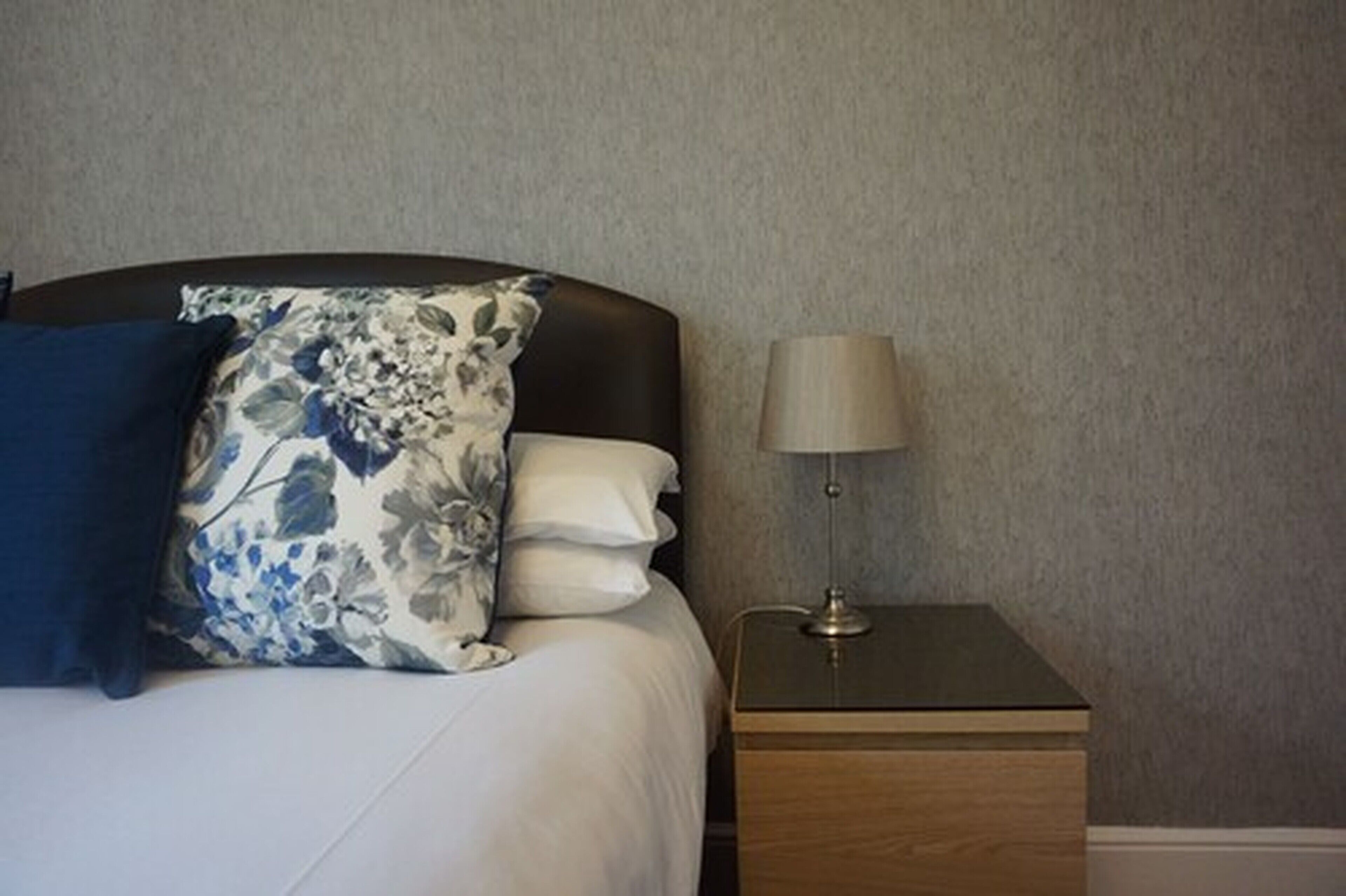 A neatly made bed with a floral pillow, a plain pillow, and a bedside table with a lamp.