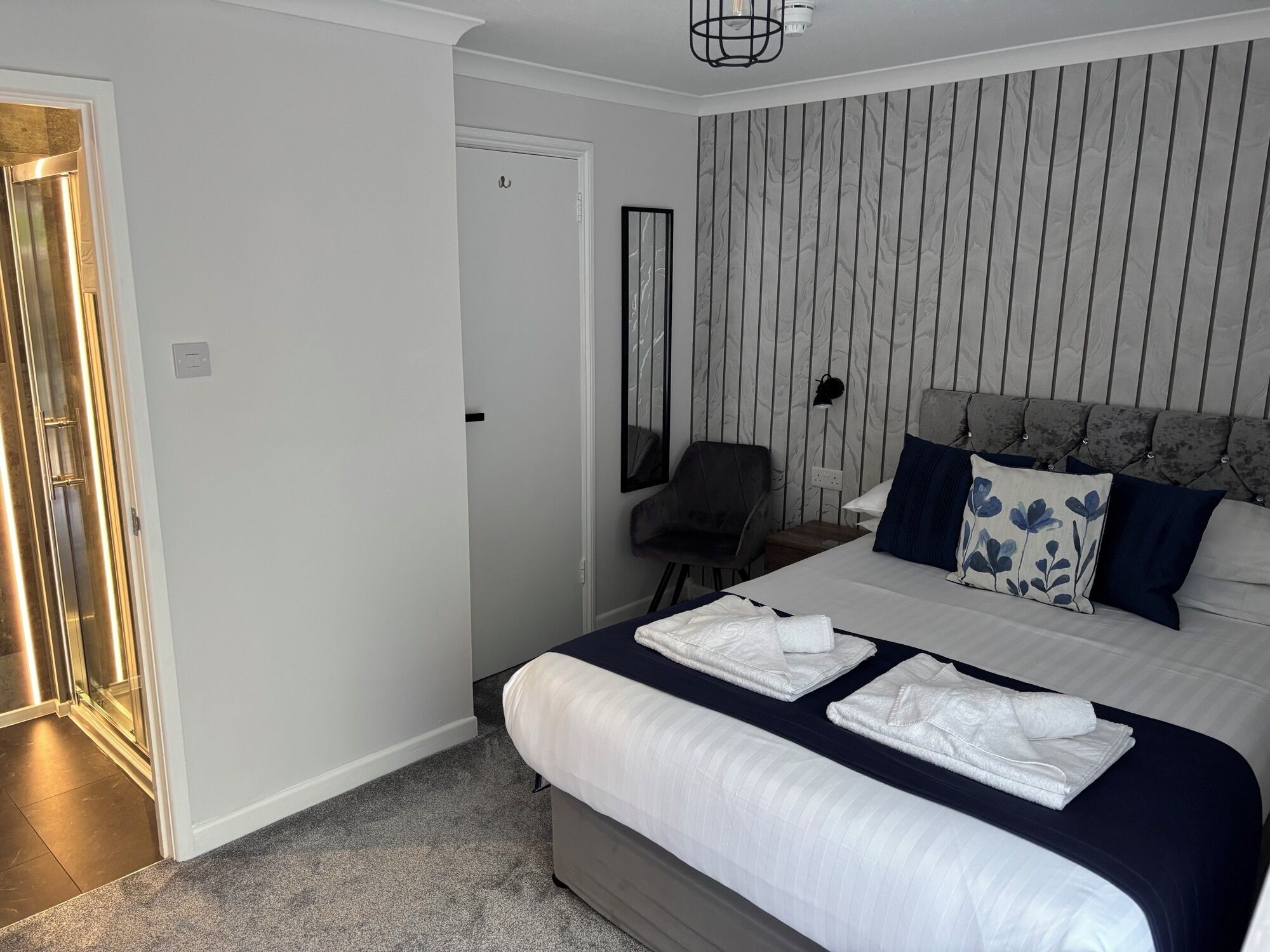 A hotel room with a bed, a chair, a mirror, and a door.