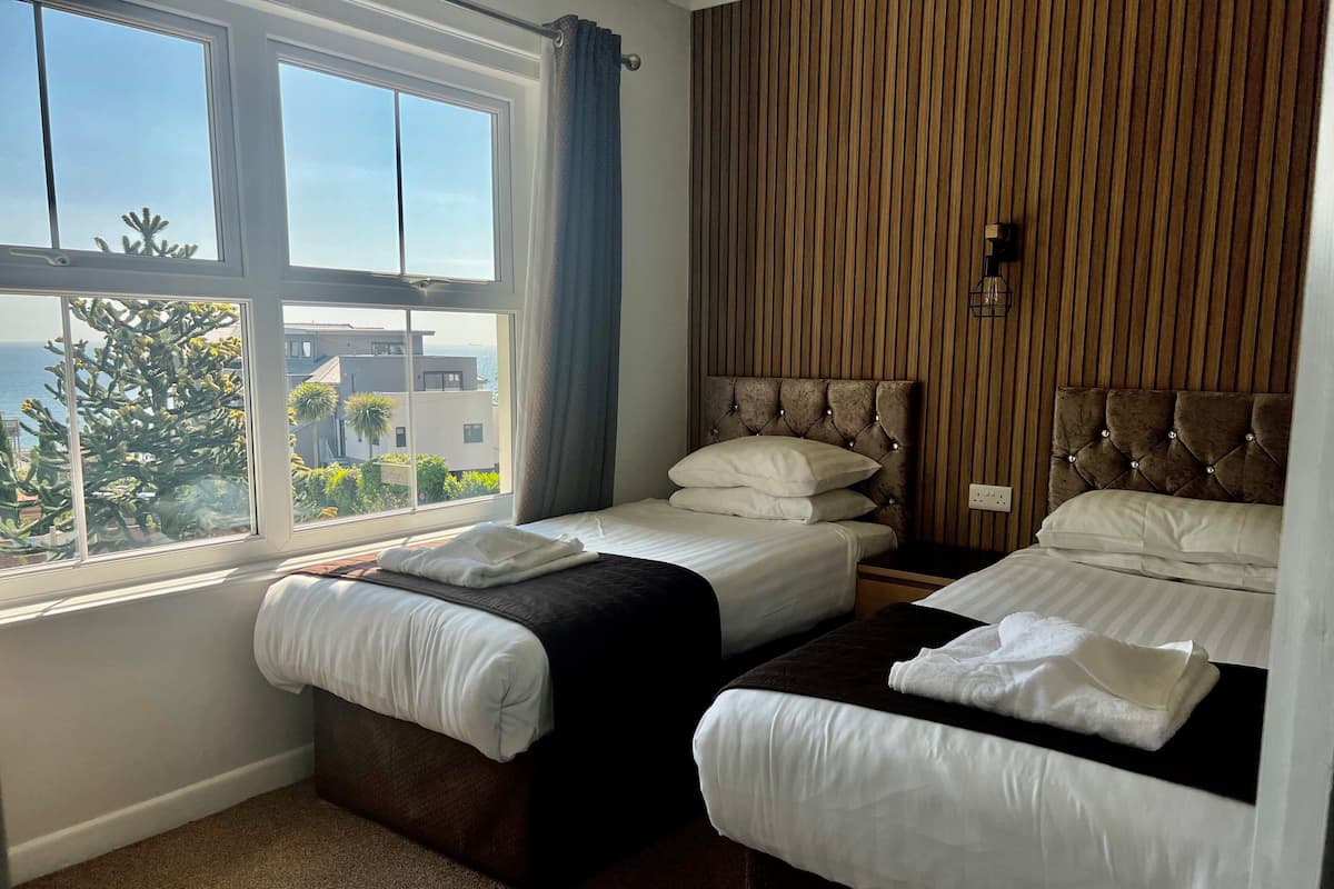 Habitación de hotel con dos camas, un ventanal con vistas a edificios y árboles, y un panel de pared de madera.