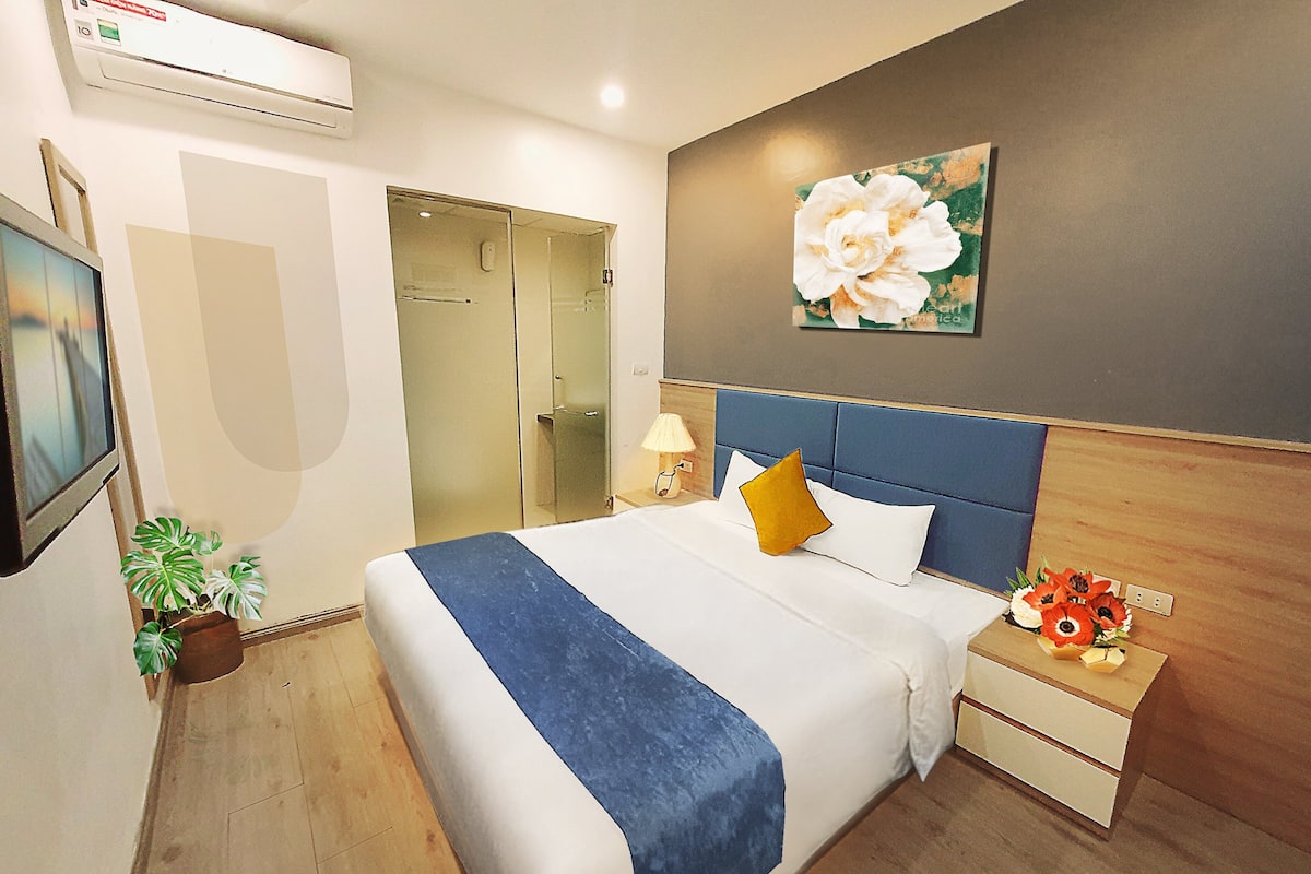 Een hotelkamer met een bed, nachtkastje, lamp en een plant in pot.