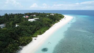 An aerial view of a tropical beach with a white sandy shore, clear turquoise waters, and dense green vegetation.