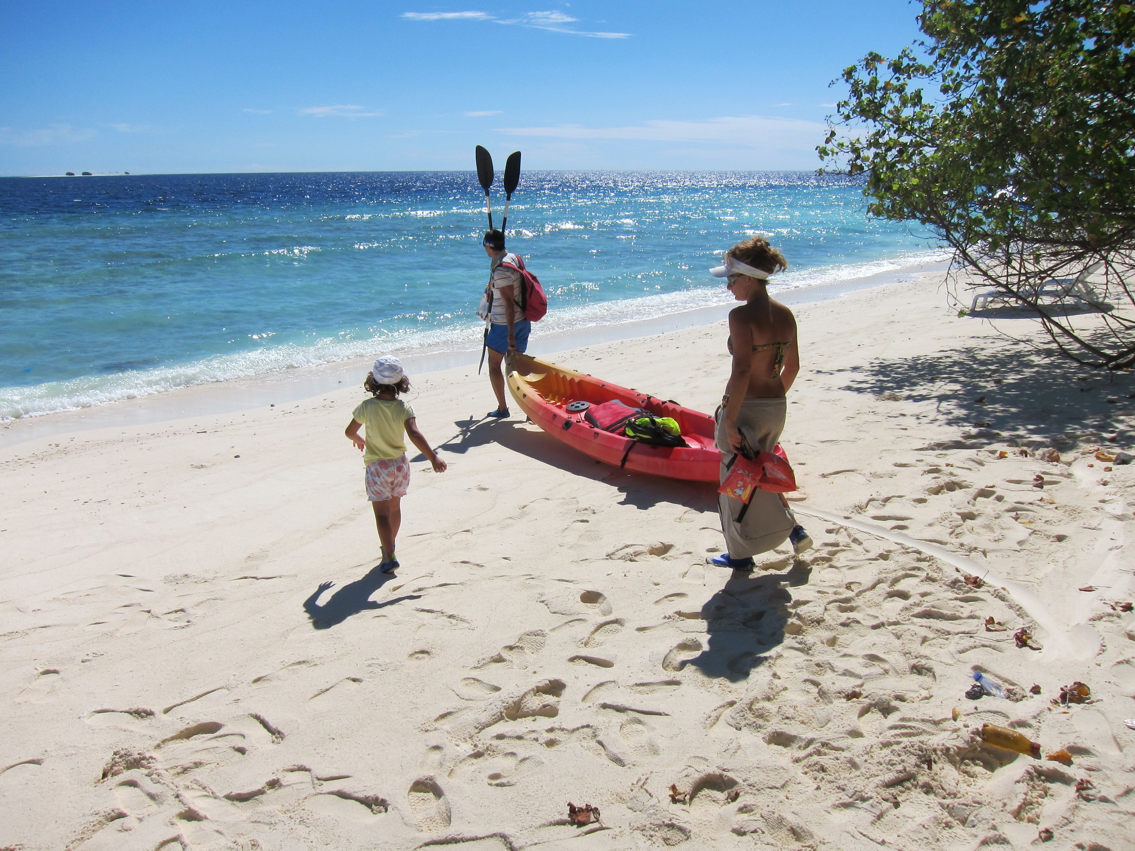 En sandstrand med fotspår, en röd kajak och en person som håller i paddlar.