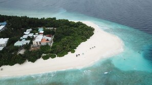 An aerial view of a tropical island with a sandy beach, clear turquoise waters, and a cluster of buildings with green roofs.