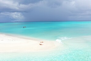 A beach with clear turquoise water, a boat, and two people lying on the sand. - SeaLaVie Inn (Ukulhas)