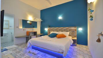 Une chambre à coucher moderne avec un grand lit, une table de chevet, un miroir et une salle de bain visible à travers une porte ouverte.