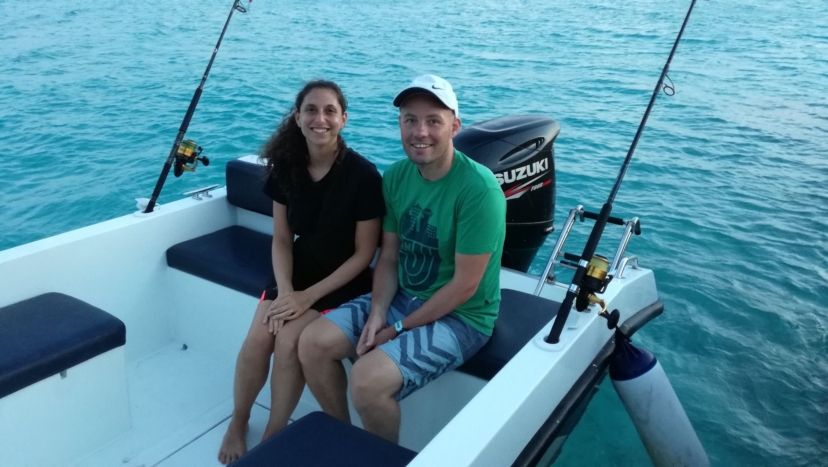 Two people on a boat with fishing rods, a Suzuki outboard motor, and a calm sea.