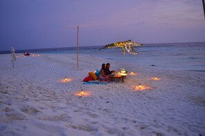 A beach setting with a couple sitting on a blanket, a small table with candles, and a decorative arch.