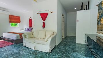 A hotel room with a bed, a white sofa, a red curtain, a ceiling fan, and a marble floor.