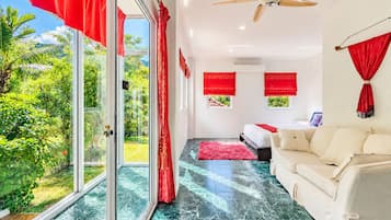 Une chambre moderne avec une porte vitrée donnant sur un balcon, un ventilateur de plafond et un lit agrémenté de rideaux rouges.