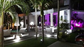 An outdoor lounge area with seating and a pool, surrounded by palm trees and illuminated by ambient lighting. - Tropicale Villa (Rawai)