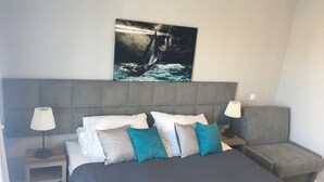 A neatly made bed with a grey headboard, white and teal pillows, and a grey blanket. There is a small bedside table with a lamp on each side of the bed. - Pensjonat Azul (Kolobrzeg)