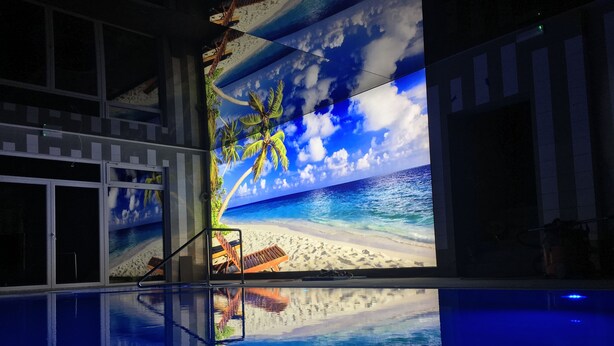 A swimming pool with a reflective surface and a large digital screen displaying a beach scene. - Pensjonat Azul (Kolobrzeg)