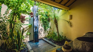 A serene garden with a stone fountain, lush greenery, and a thatched ceiling. - Minabali Bunga'lo (Tulamben)