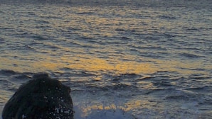 A sunset over the ocean with waves crashing onto rocks. - Minabali Bunga'lo (Tulamben)