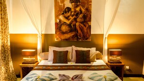 A hotel room with a bed, pillows, a painting, and two bedside lamps. - Minabali Bunga'lo (Tulamben)